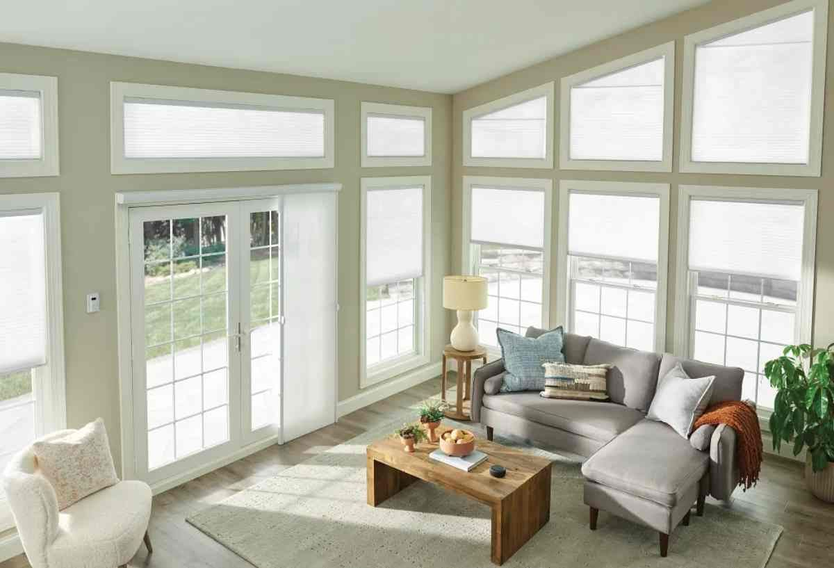 Bright sunroom with large windows, gray sectional sofa, coffee table, lamp, and white chair.