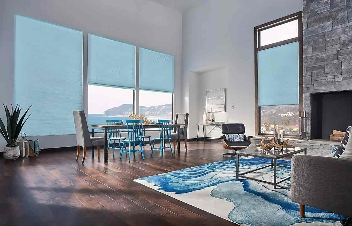 Modern living room with blue accents, large windows, dining table, sofa, and fireplace overlooking water