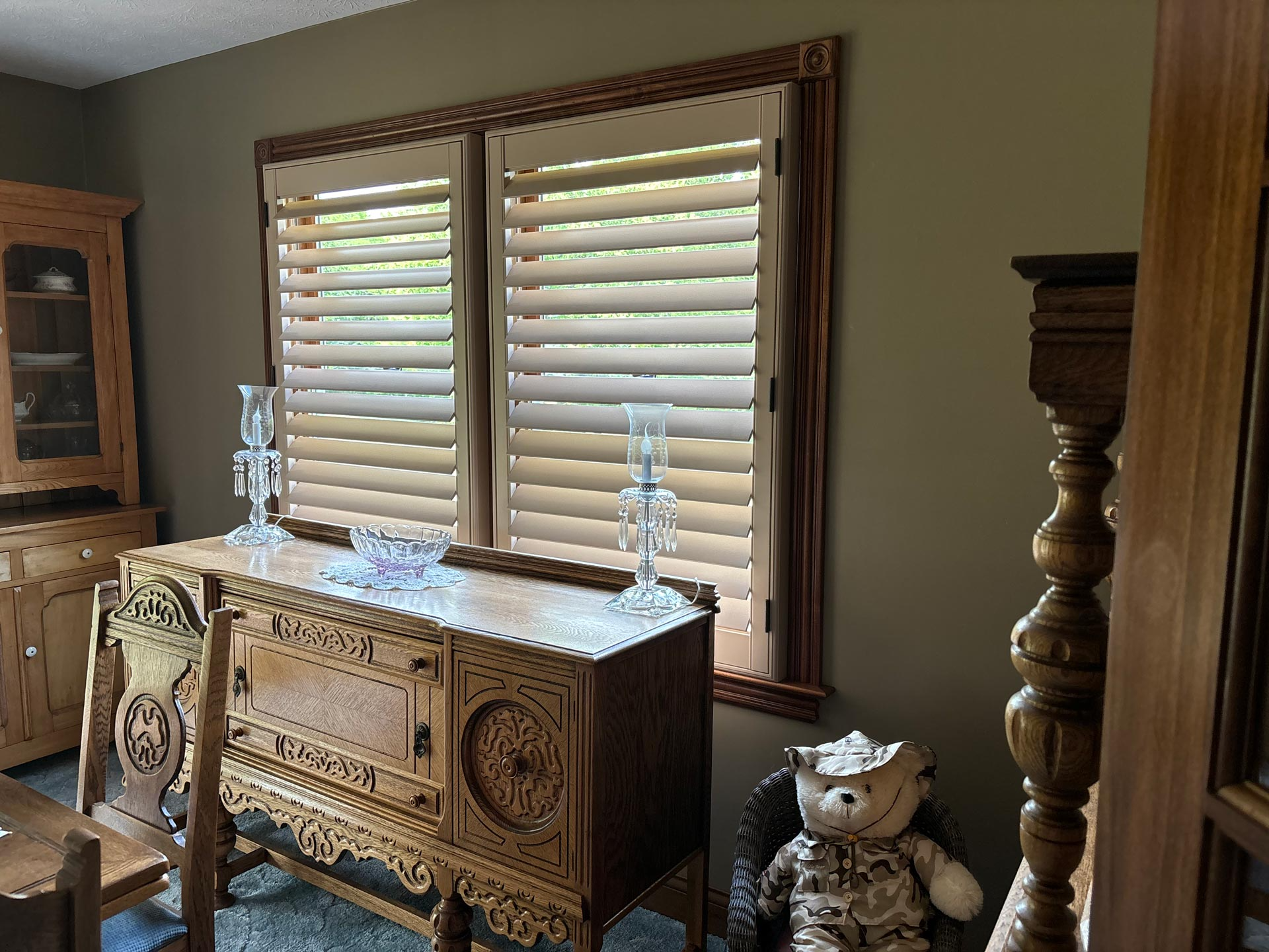 Ornate wooden cabinet and decor in a warmly lit room with shuttered windows and a side table