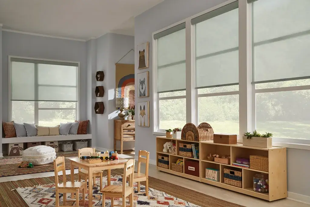 Bright classroom with tables, shelves, rugs, and large windows letting in daylight.