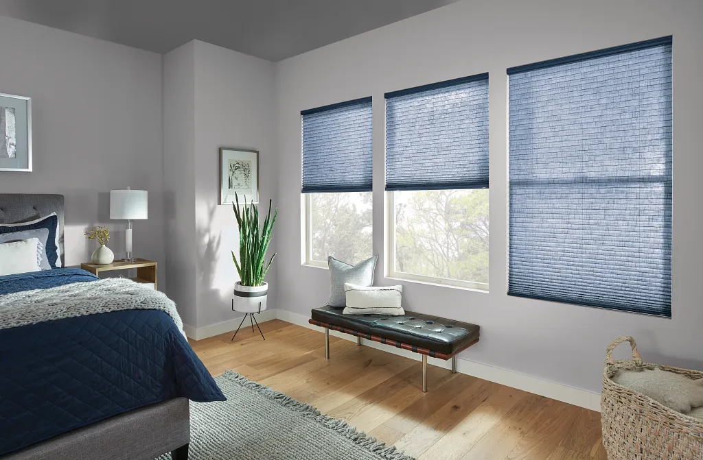 Bright bedroom with blue bedding, large windows with blue blinds, and a bench by the window.