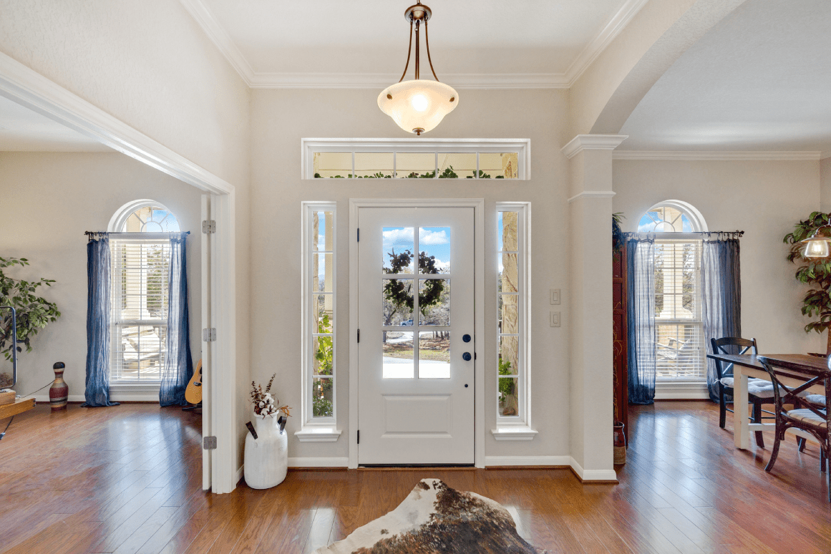 Bright foyer with white double doors, hardwood floors, chandelier, and blue drapes on side windows