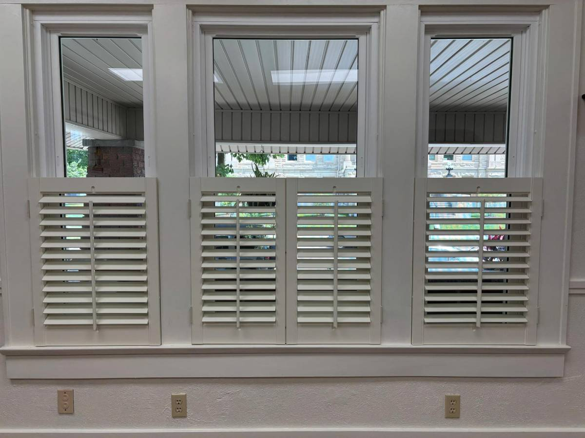 White shuttered window with three panes and a view of a covered patio outside