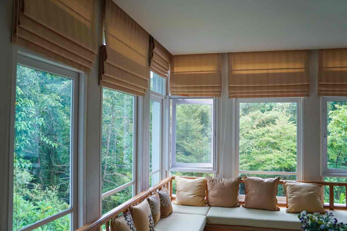 Sunlit window seat with beige cushions overlooking lush green trees