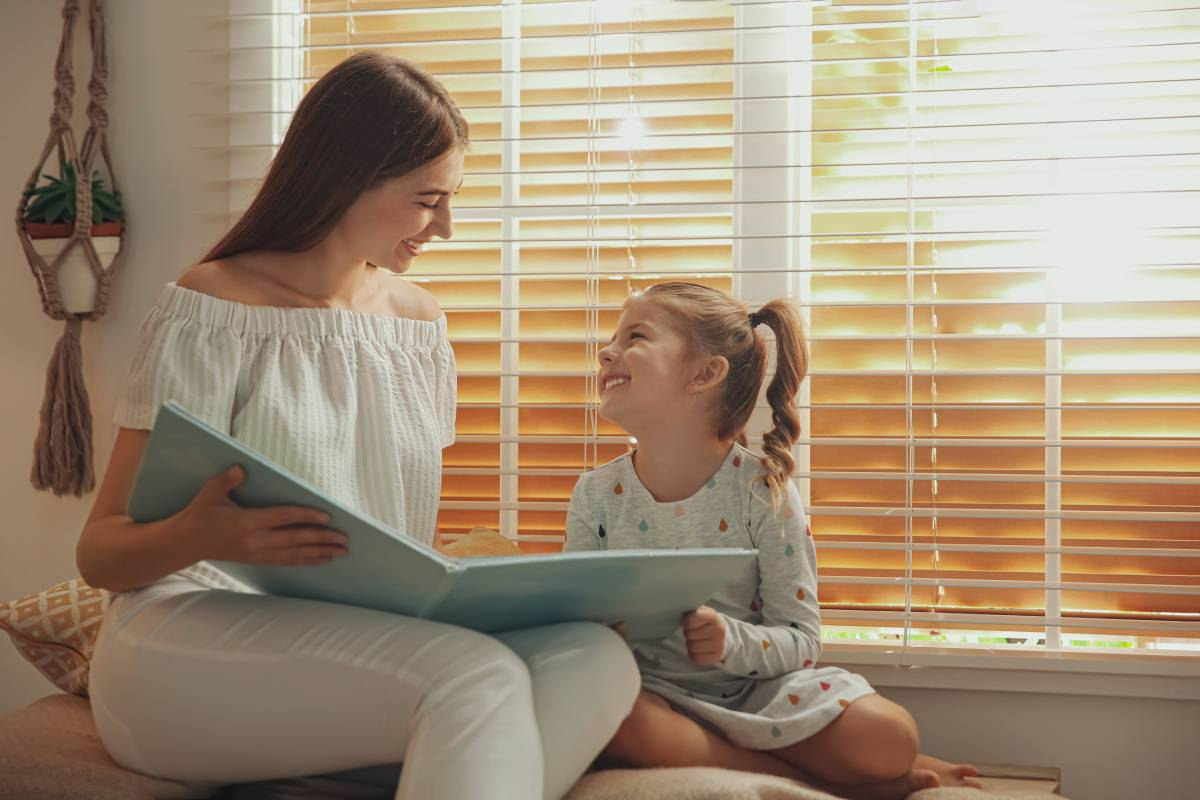 Woman and child reading a book together by a sunlit window