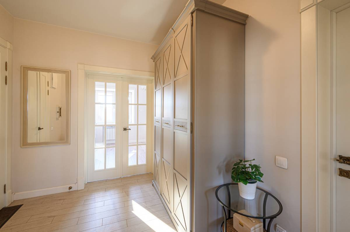 Bright entryway with French doors, tall wardrobe, wall mirror, and small table with a plant.