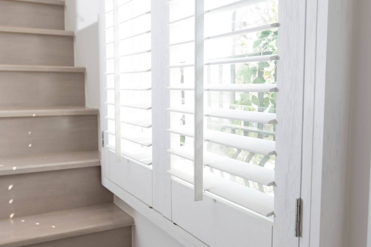White plantation shutters beside a beige staircase in a bright interior