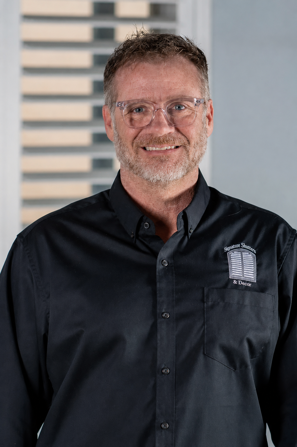 Smiling person in glasses and a black turtleneck against a light background