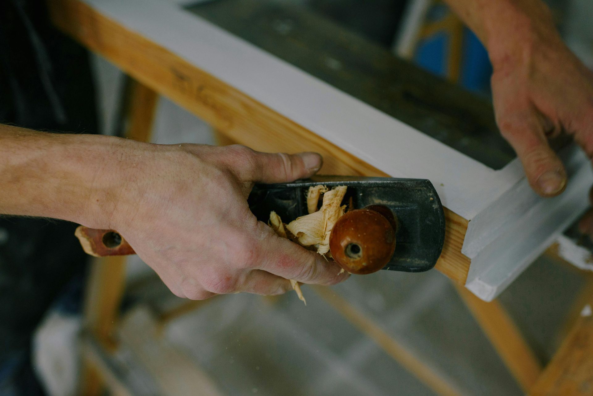 Hands using a hand plane to shave wood on a workbench