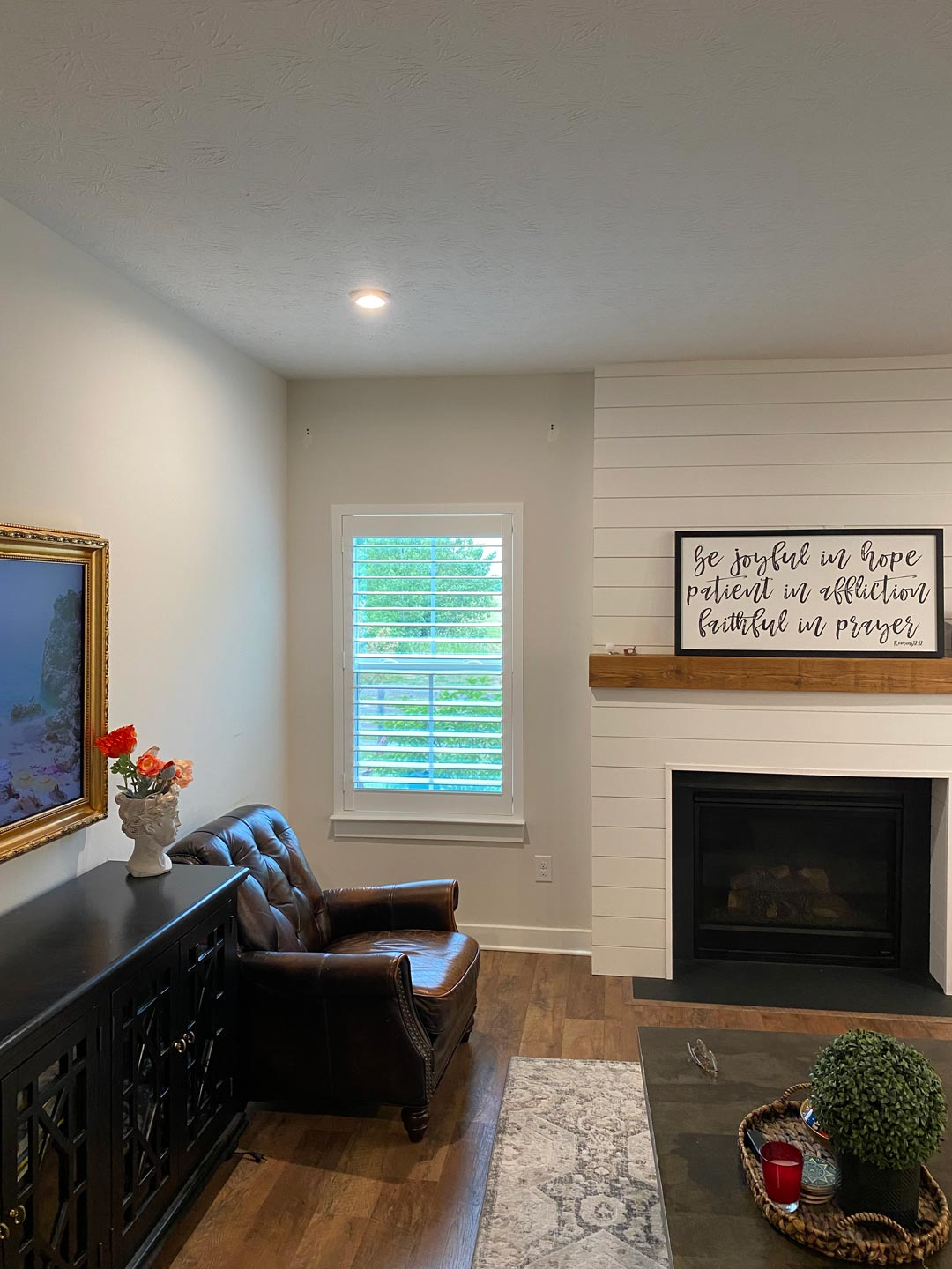 Cozy living room with leather chair, fireplace, window blinds, framed art, and dark wood furniture.