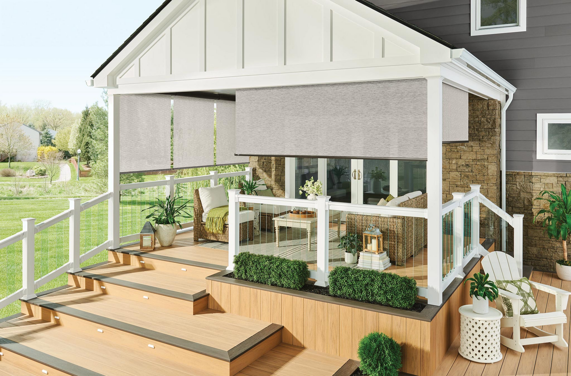 Covered wooden porch with railing, steps, potted plants, and wicker chairs on a bright sunny day