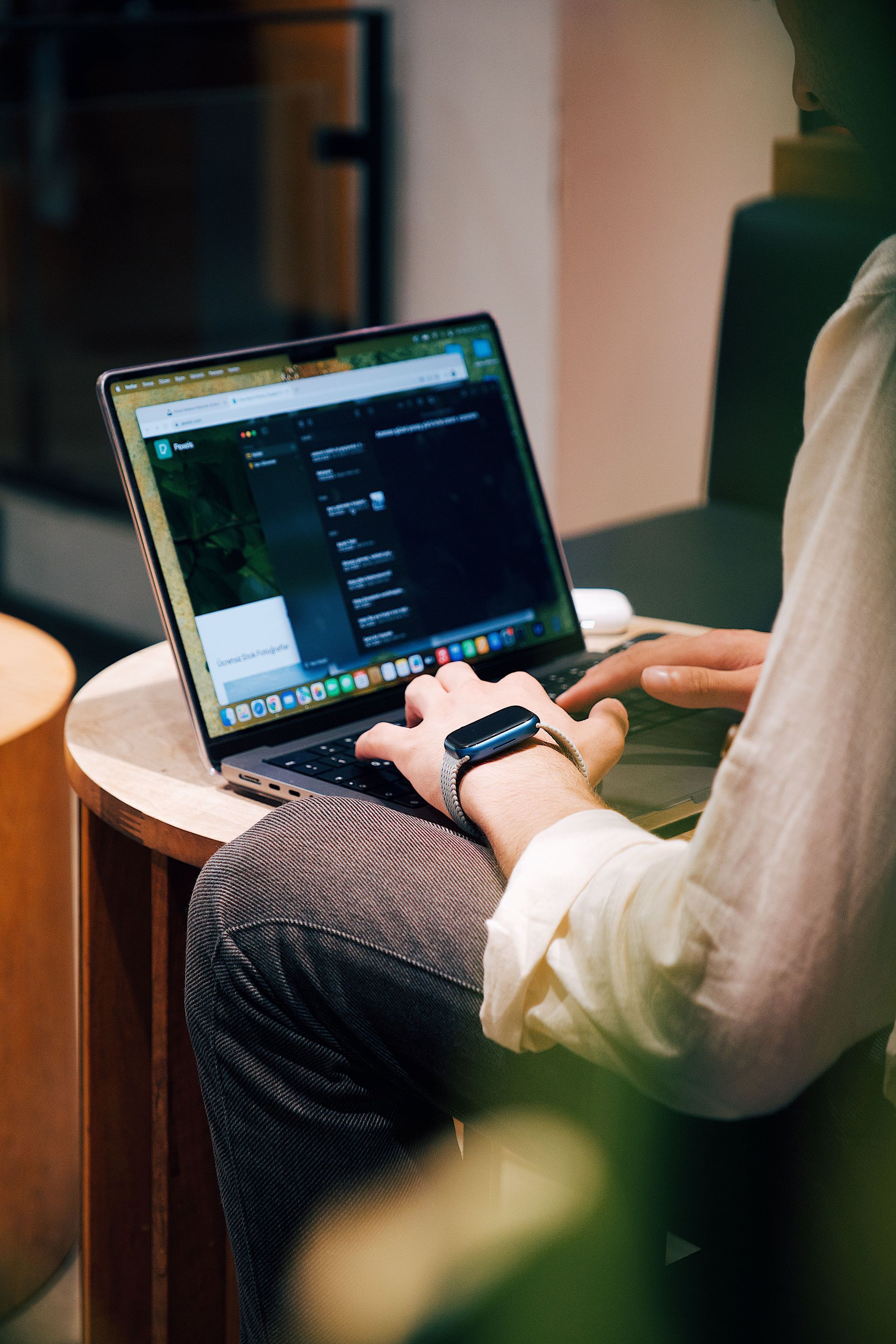 Person using a laptop at a round table, typing on a dark-screened computer in a cozy indoor setting