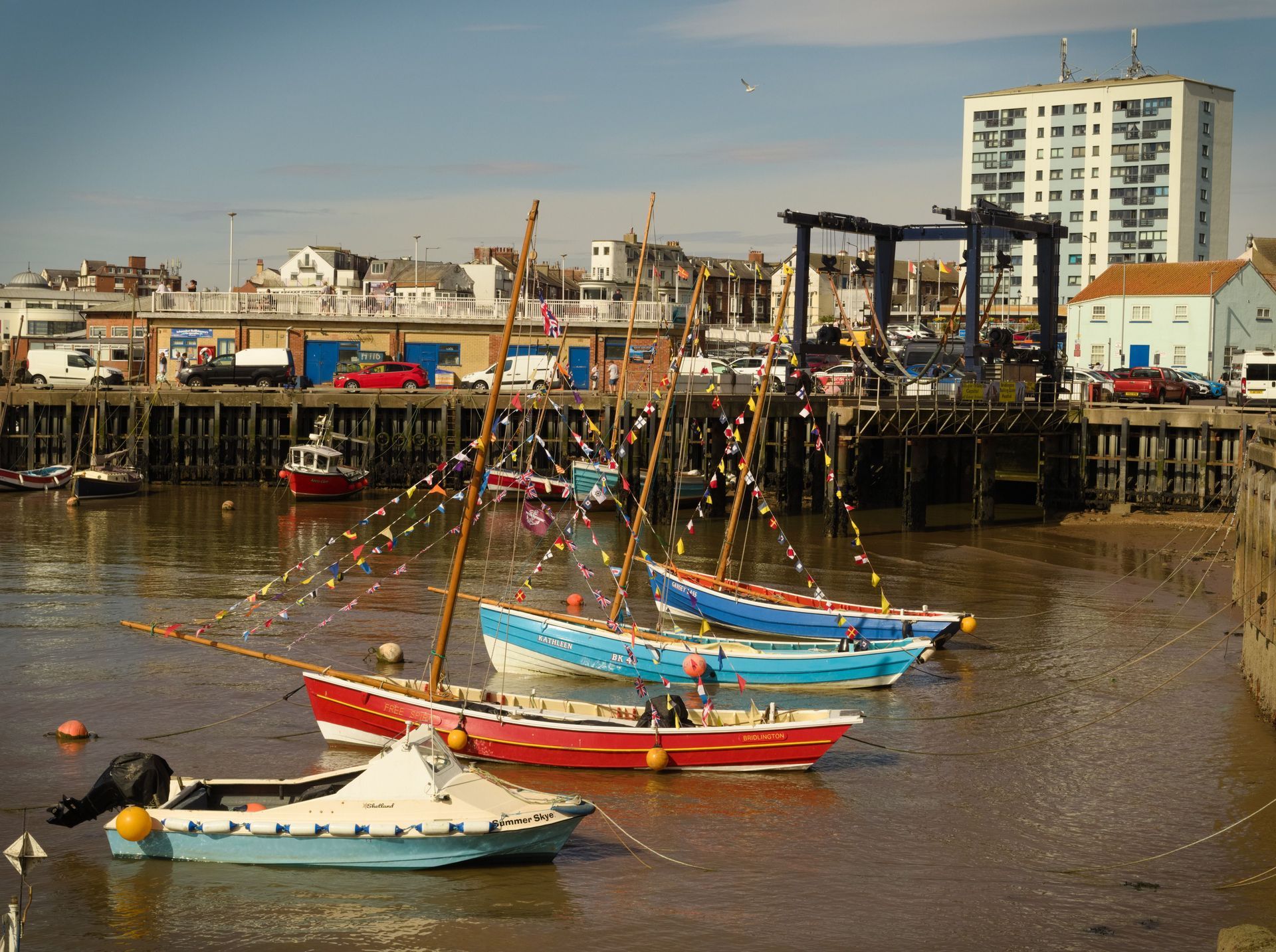 Colorful sailboats moored in a harbor with a waterfront town and buildings in the background.