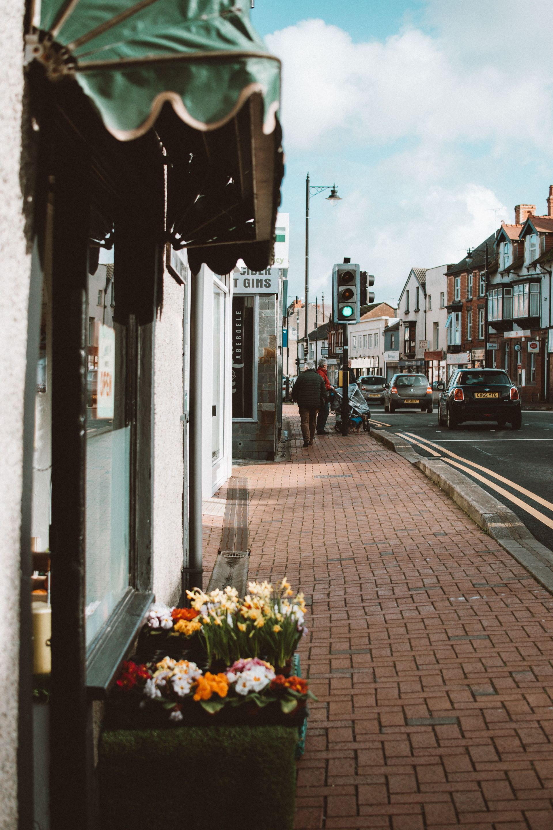 Sidewalk with flower planter and storefronts along a busy city street under a cloudy sky