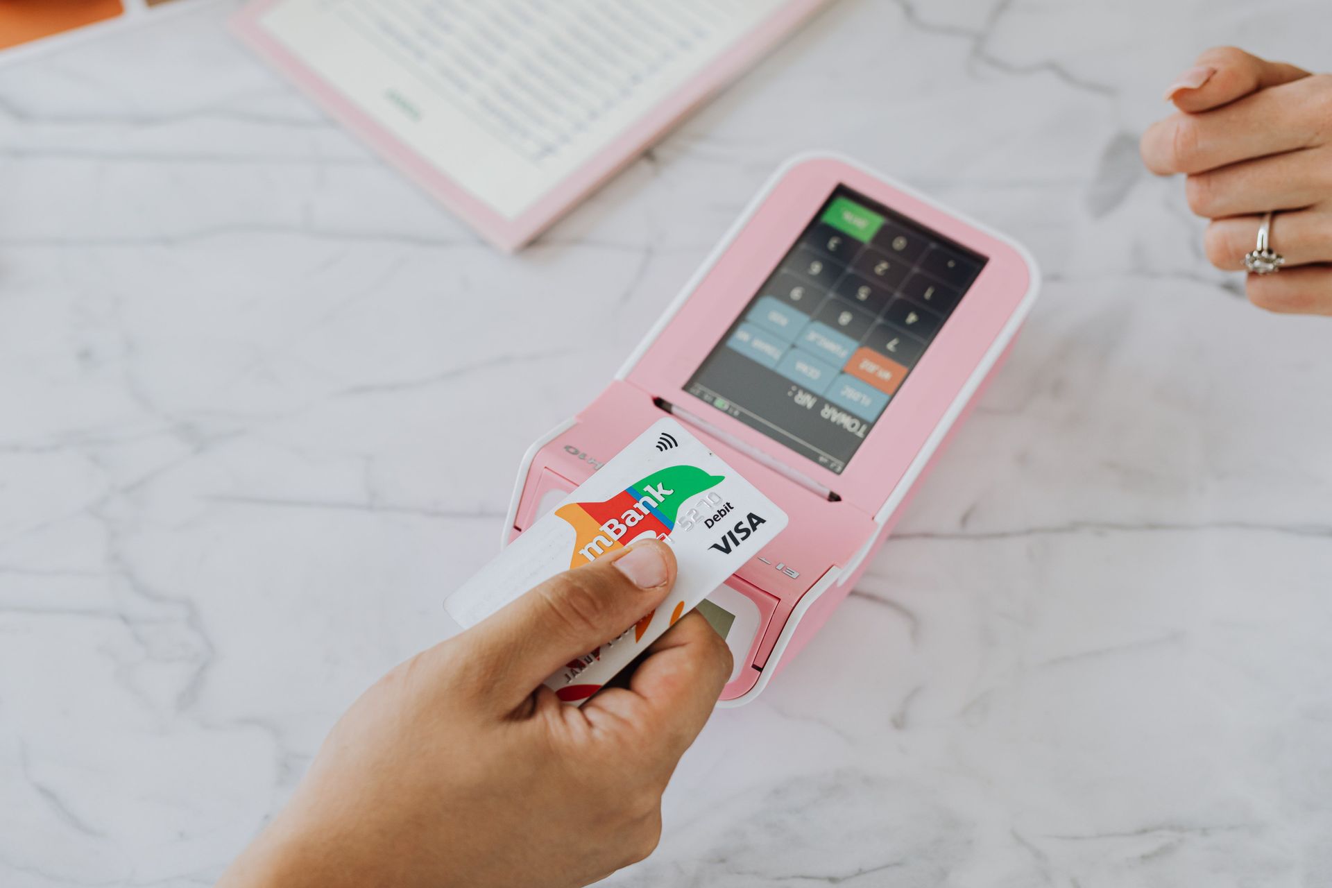 Hands inserting a card into a pink card reader on a white desk