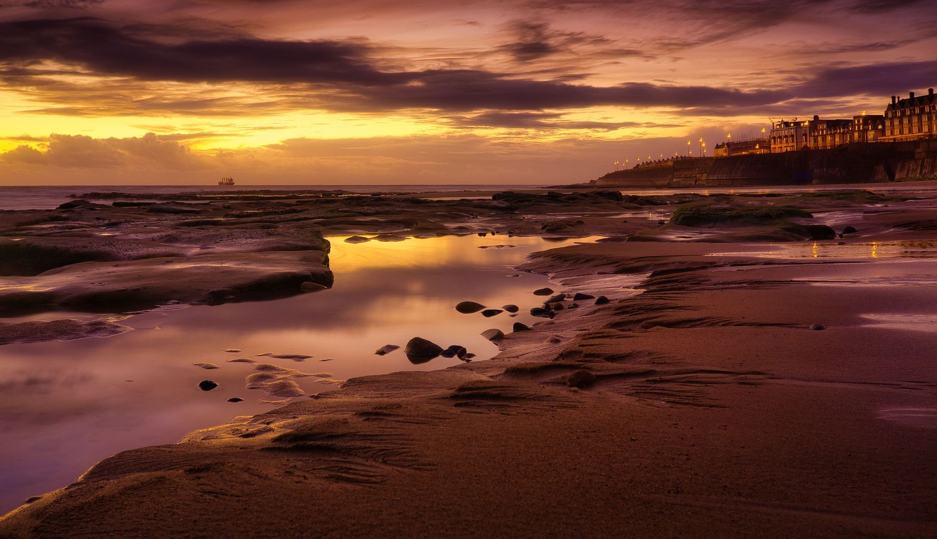 Sunset over a rocky beach with purple-orange sky and calm tide pools reflecting the light