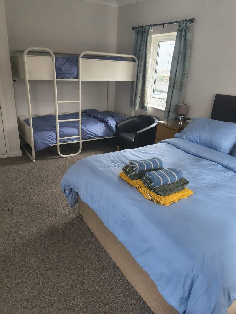 Small room with bunk beds, a bed with blue bedding, and a window in the corner.