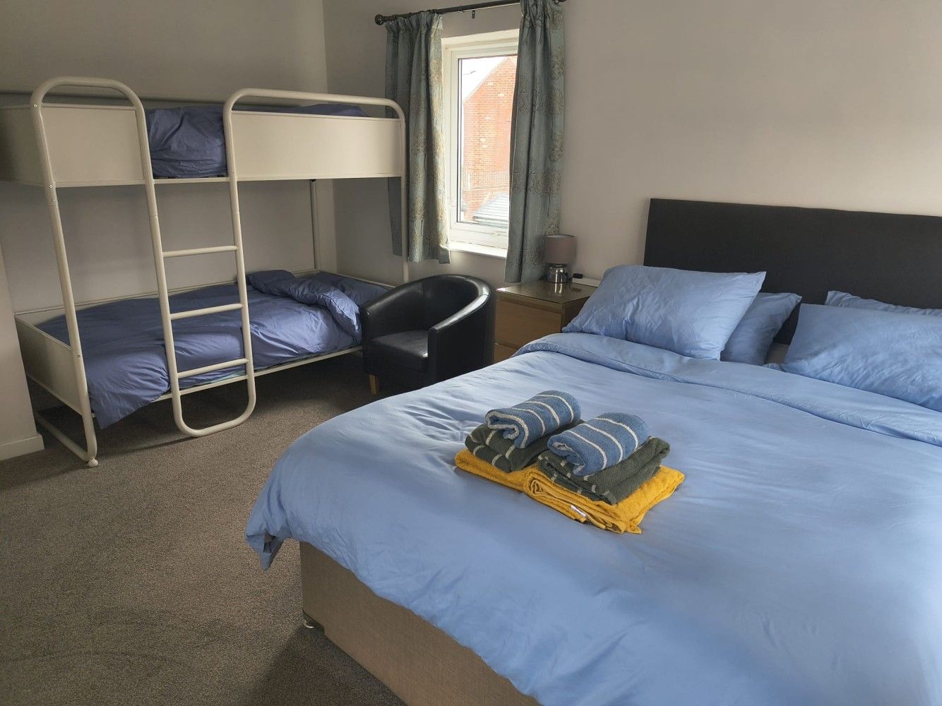 Hotel room with a queen bed, bunk beds, window, and folded towels on the bed.