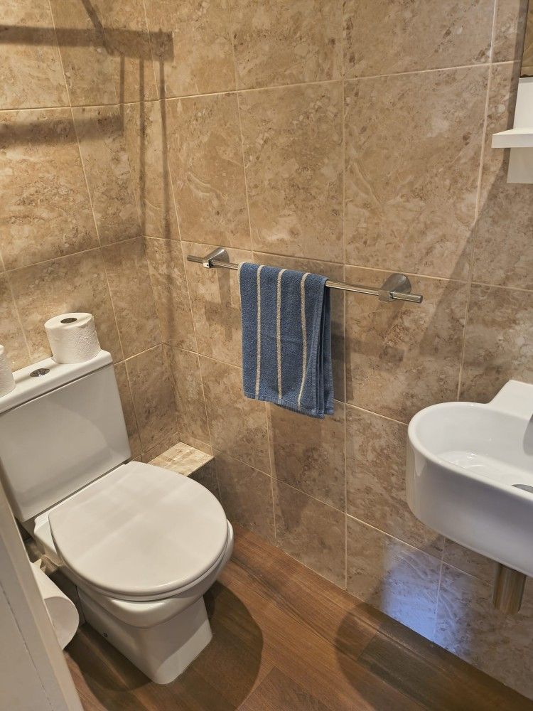 Small bathroom with toilet, sink, towel rack, and stone tile walls.