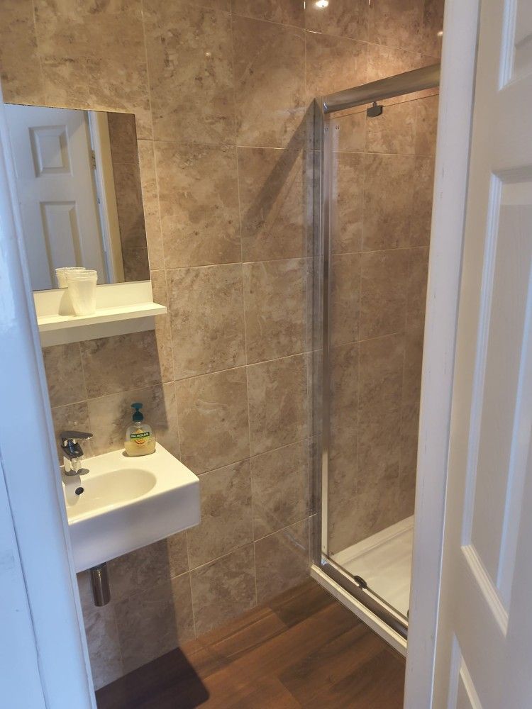 Small bathroom with a sink, mirror shelf, and glass shower enclosure with brown tiled walls.