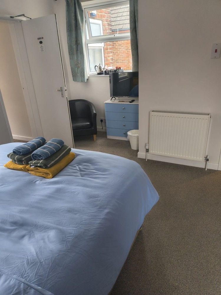 Bedroom with bed, folded towels, wardrobe, window, and blue dresser beside a radiator.