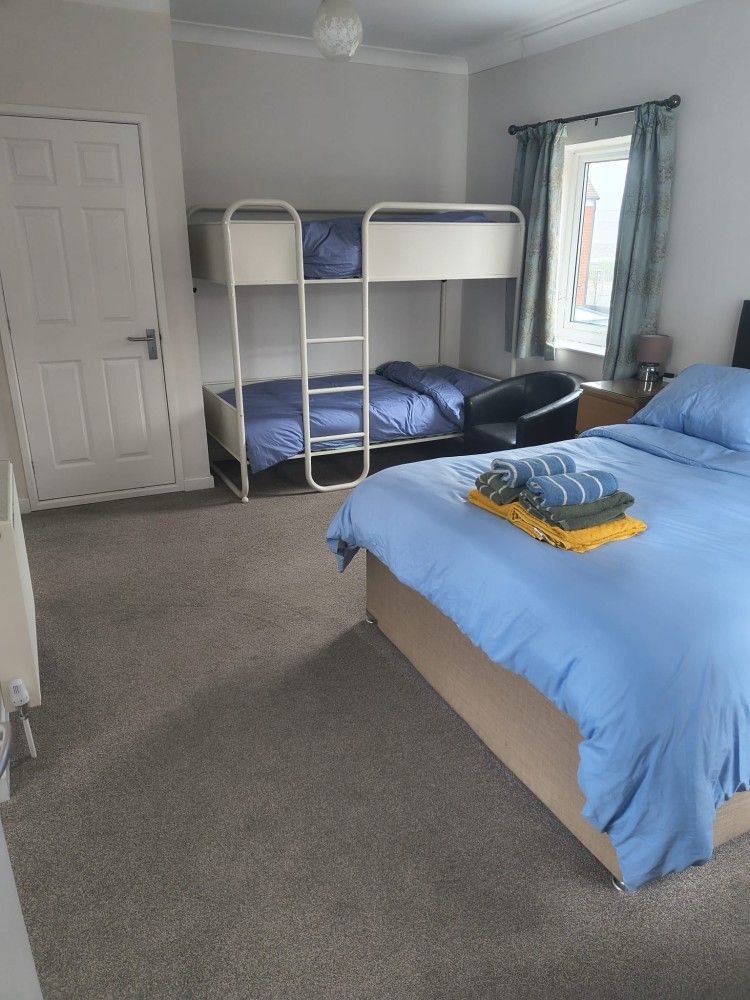 Bedroom with blue bed, bunk bed, black sofa, and window with curtains