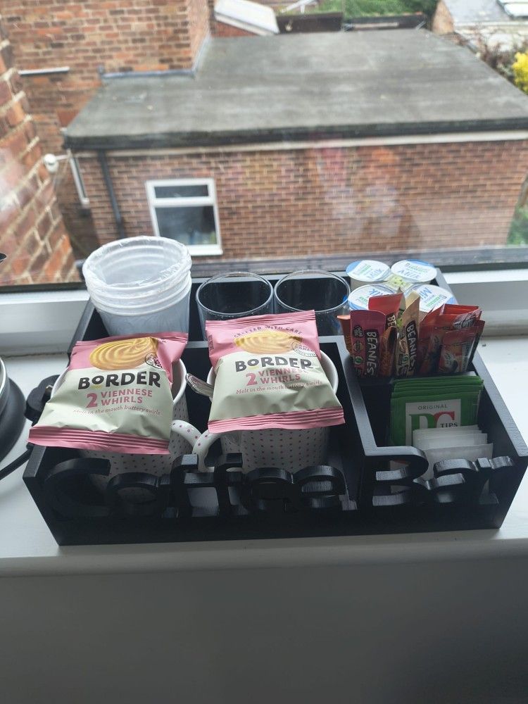 Window ledge with snack boxes, canned drinks, and cups in front of a brick building