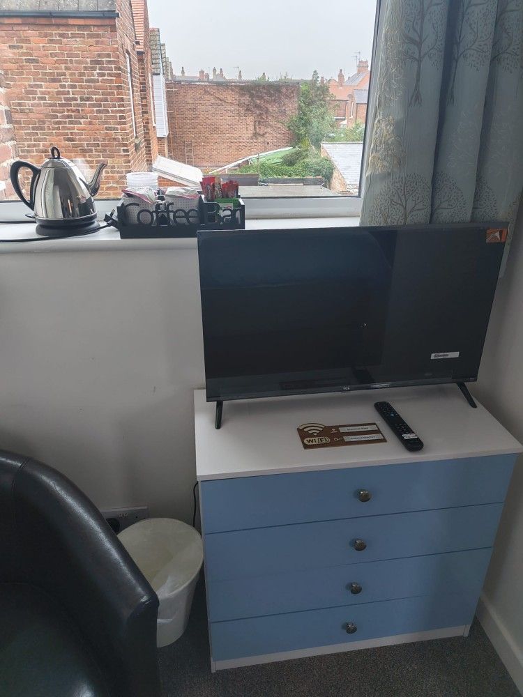 Bedroom corner with a TV on a blue dresser, a black chair, and a window with city view.
