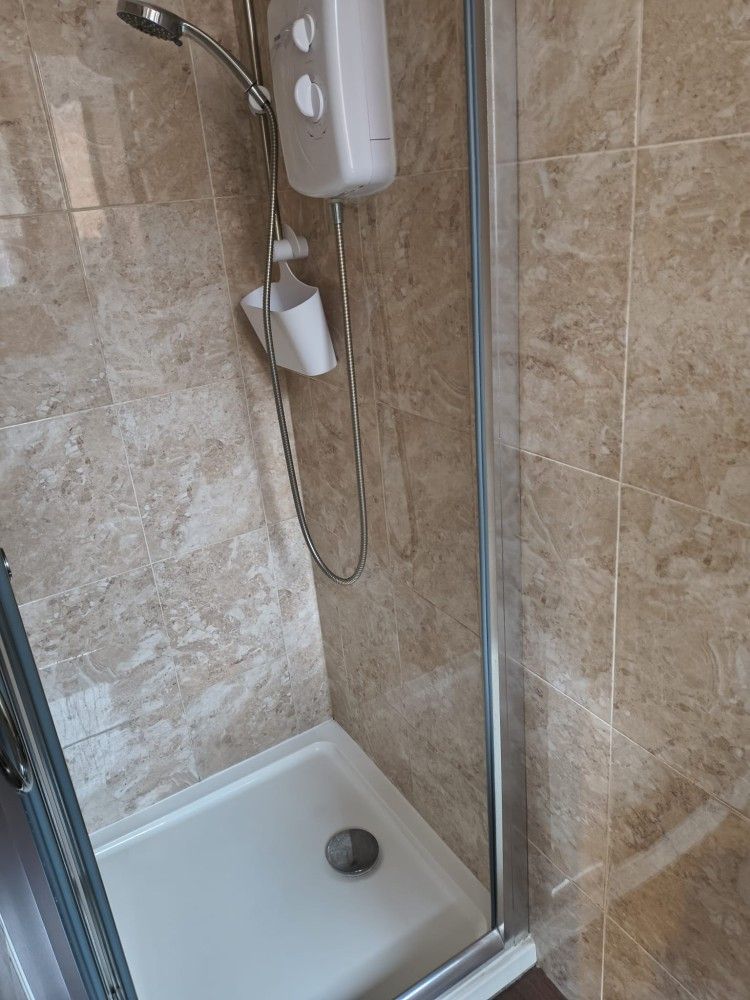 Walk-in shower with beige tile walls, glass door, and white shower bench with handheld showerhead.