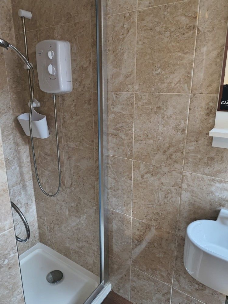 Bathroom shower stall with beige tile, wall-mounted shower fixtures, and a visible sink edge.