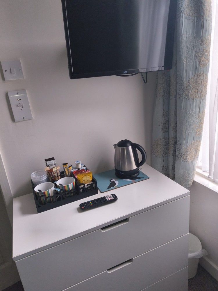 Hotel room dresser with tea and coffee tray, electric kettle, TV above, and curtains by the window