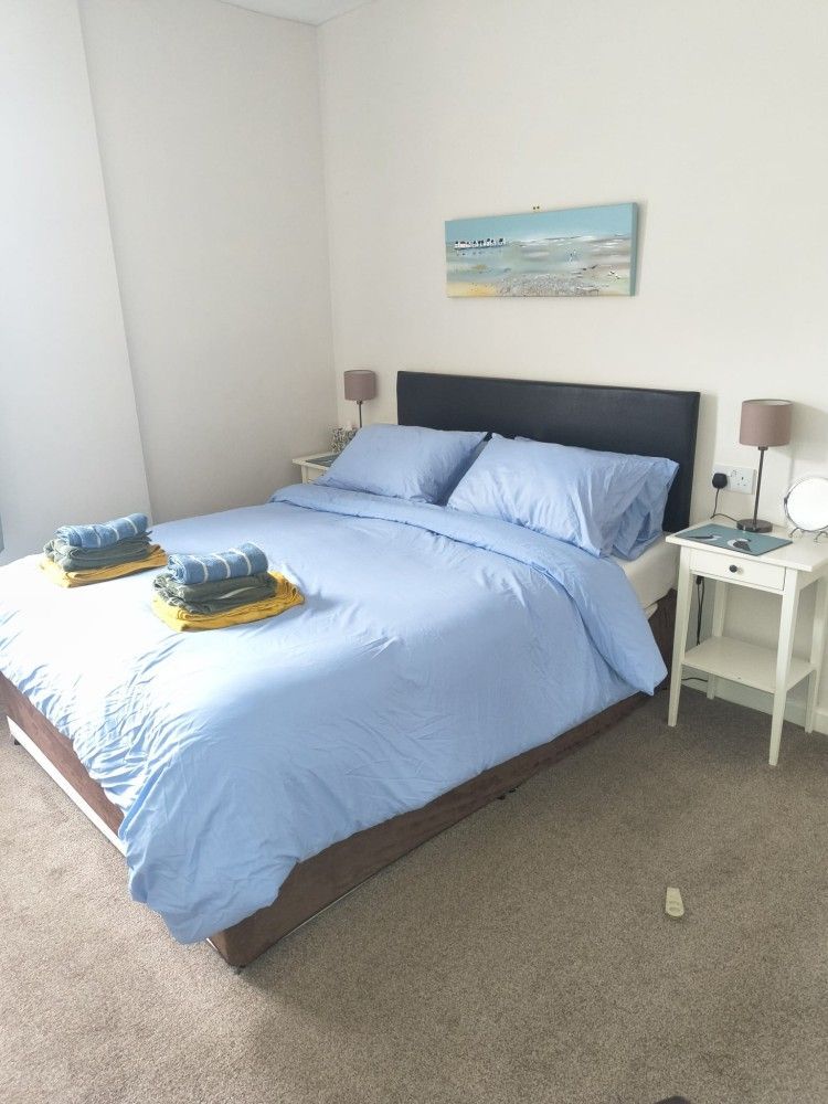 Neat bedroom with a blue bedspread, bedside tables, and a wall painting on carpeted flooring.