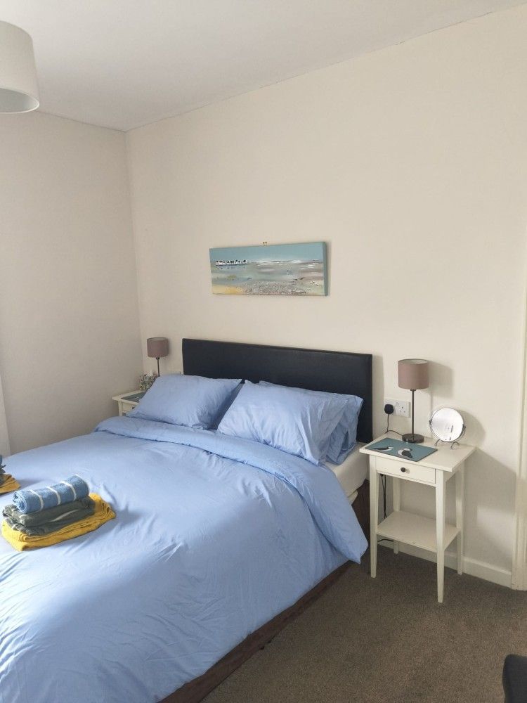 Bright bedroom with a blue bedspread, two bedside tables, and a small beach painting above the bed