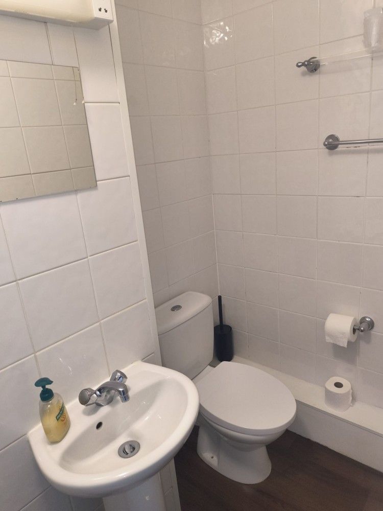 Small white bathroom with a sink, toilet, tiled walls, toilet paper holder, and cleaning bottle.