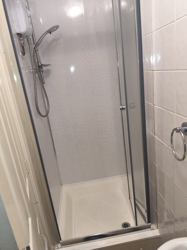 Narrow tiled shower stall with glass door and handheld showerhead.