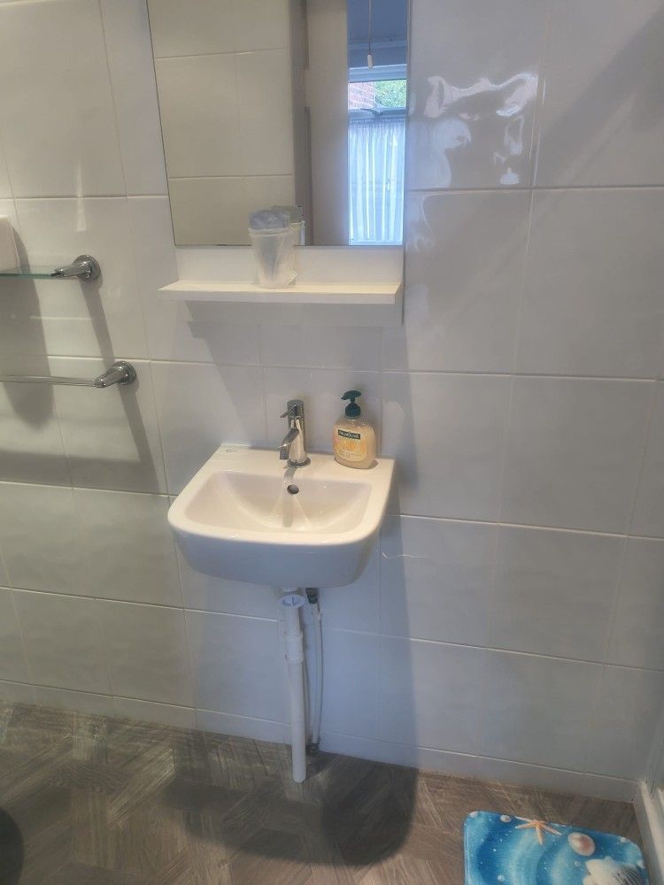 Small bathroom with wall-mounted sink, mirror shelf, and shower grab bars