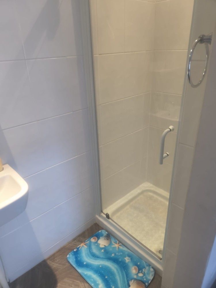 Bathroom with a glass shower enclosure, beige tile, and a blue bath mat on the floor