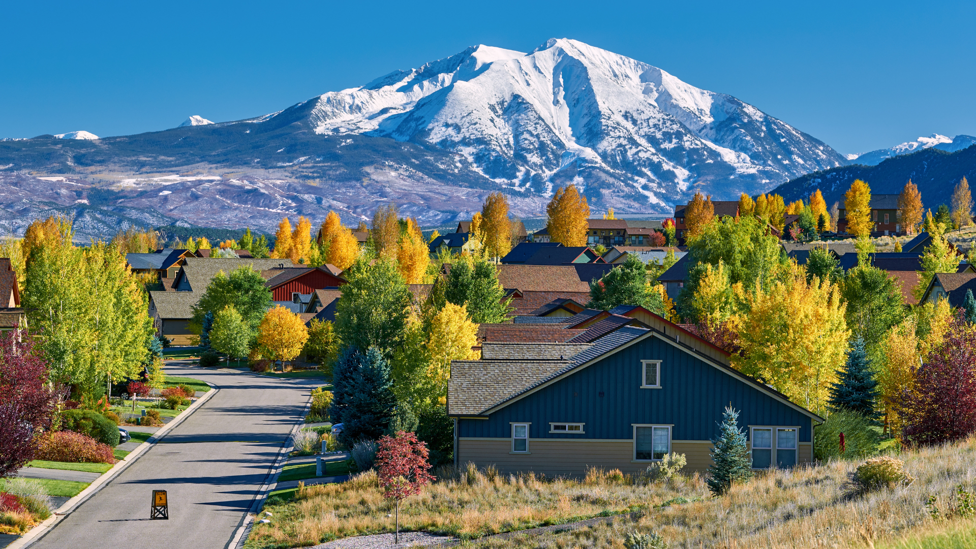 Residential street with colorful autumn trees and a snowcapped mountain in the background