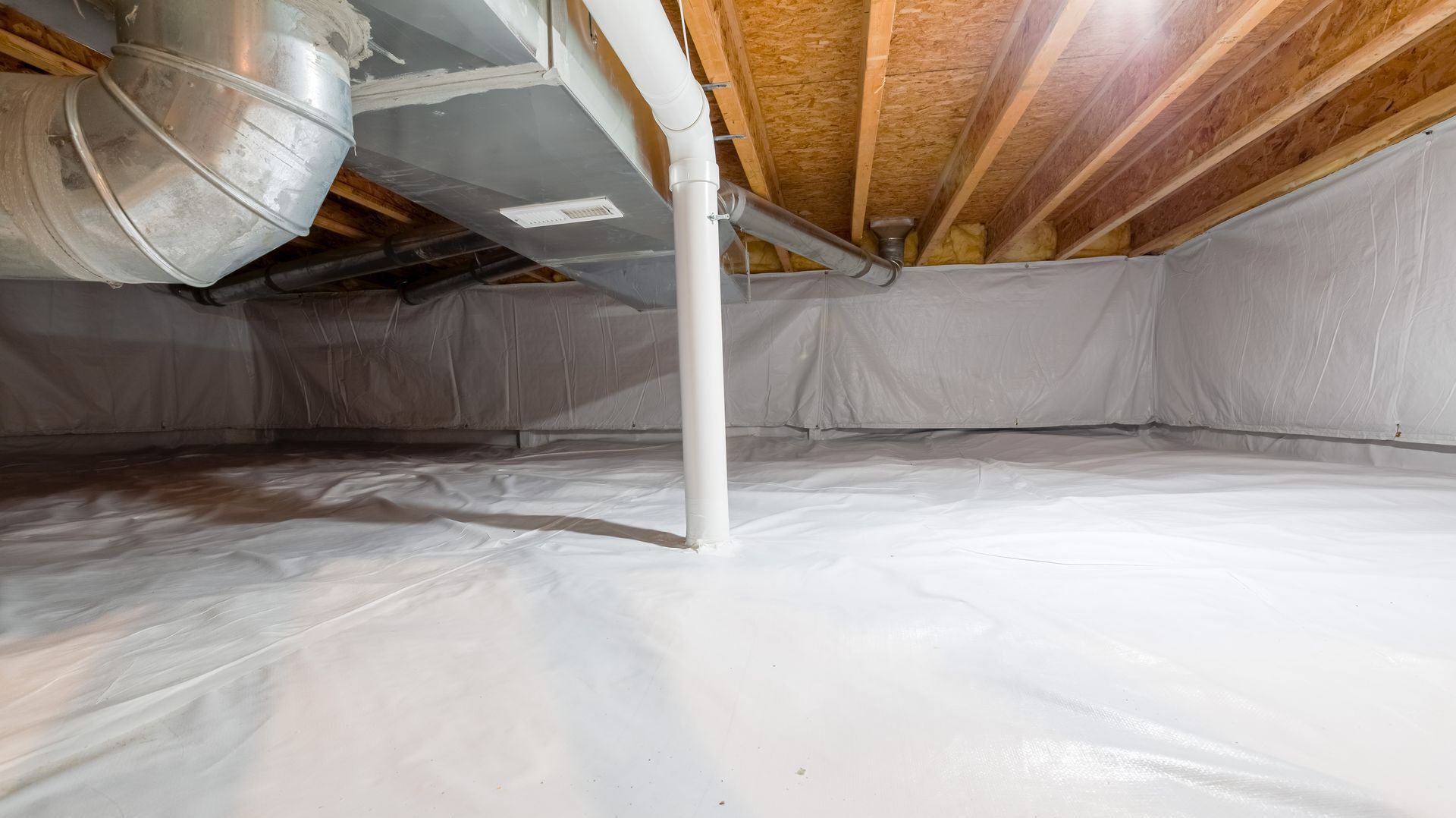 A crawl space with white vapor barrier on the walls and floor, wooden joists, and ductwork overhead.