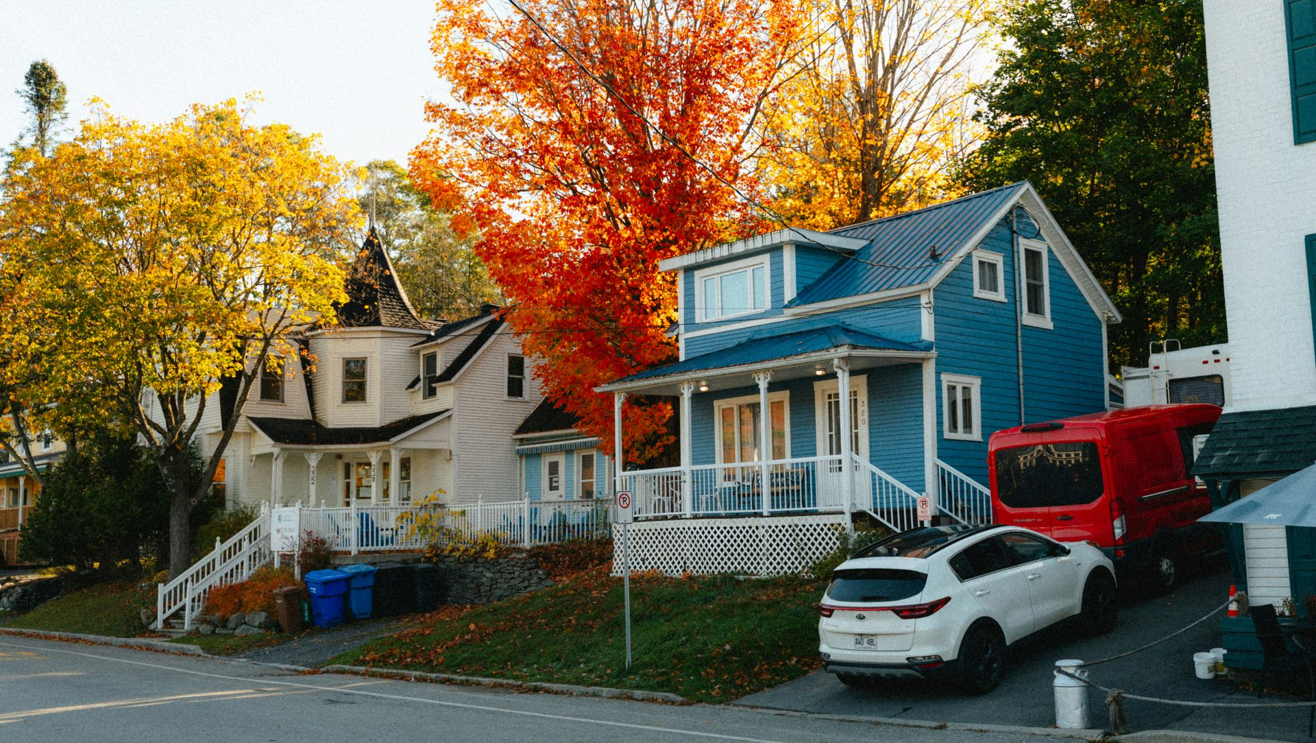 Houses with colorful autumn trees lining a street; a blue house has a white car parked in front.