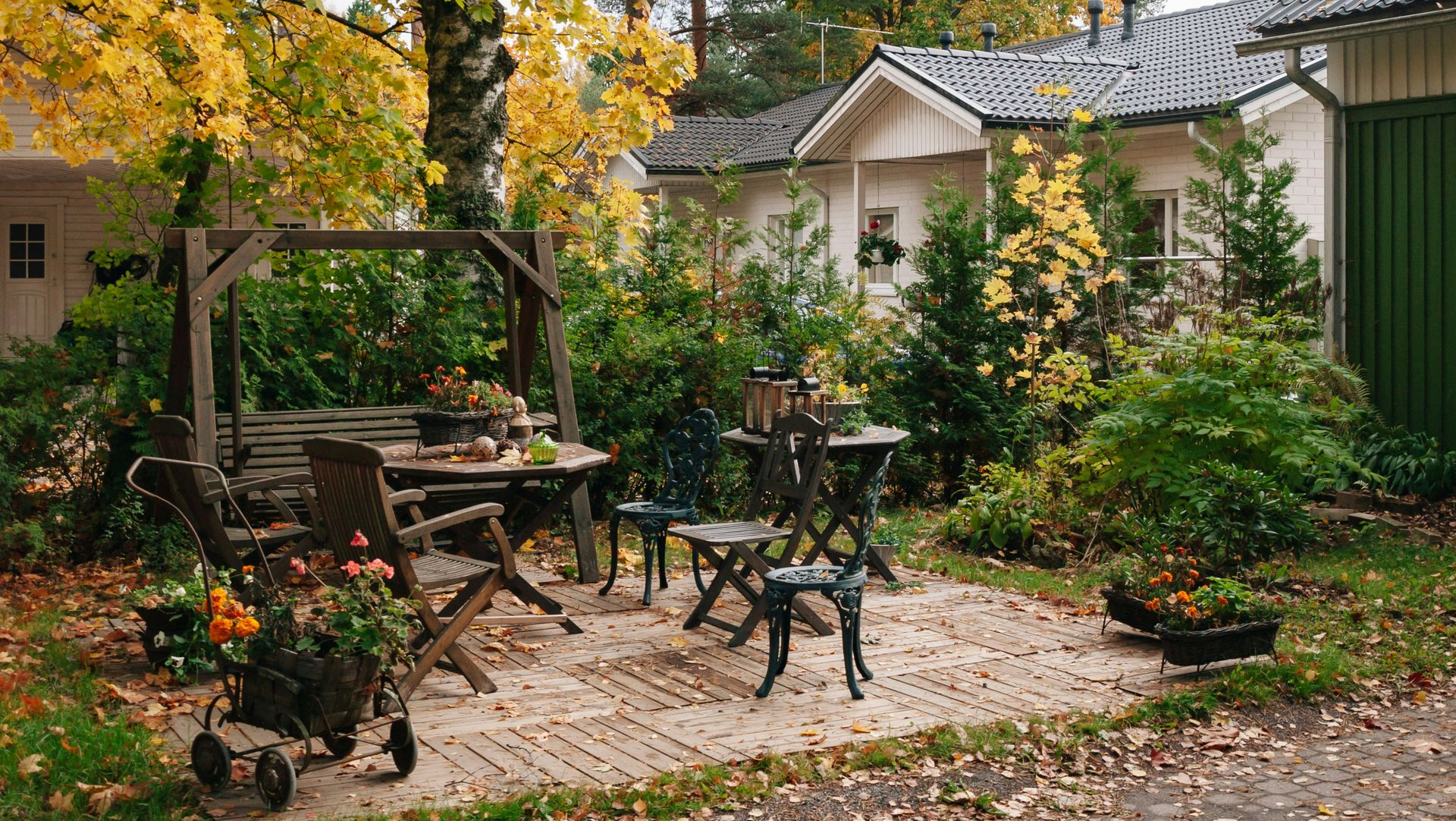 Outdoor patio with wooden furniture, surrounded by greenery and autumn foliage.