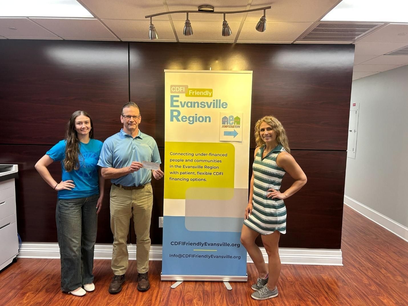 Three people posing beside a bright yellow-blue event banner in a hallway.