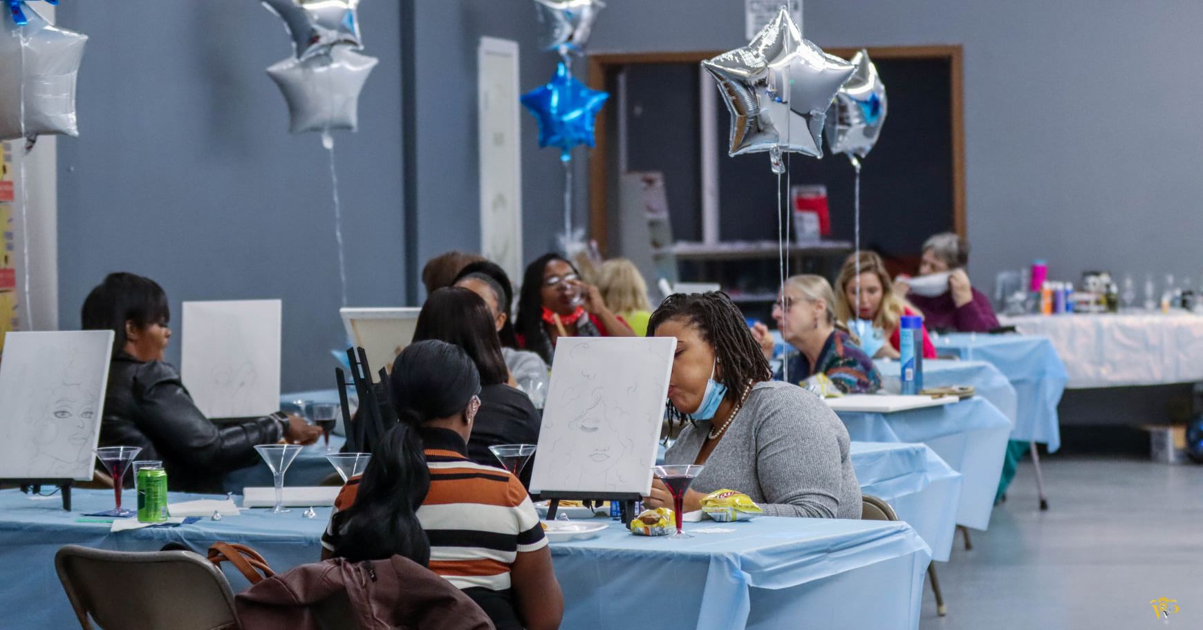 A group of people are sitting at tables in a room with balloons.