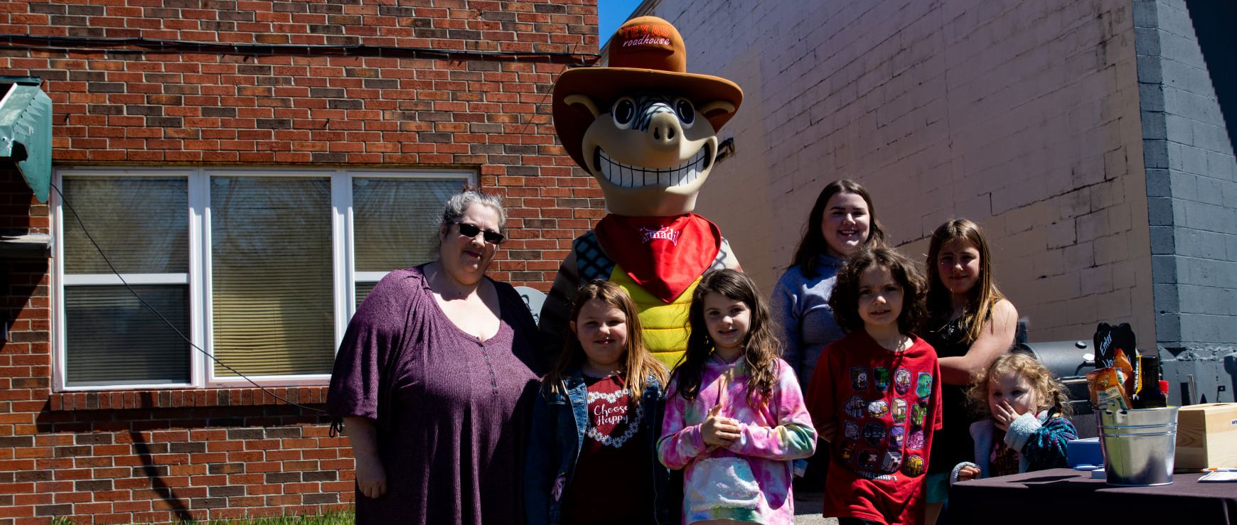 A group of people are posing for a picture with a mascot in front of a brick building.