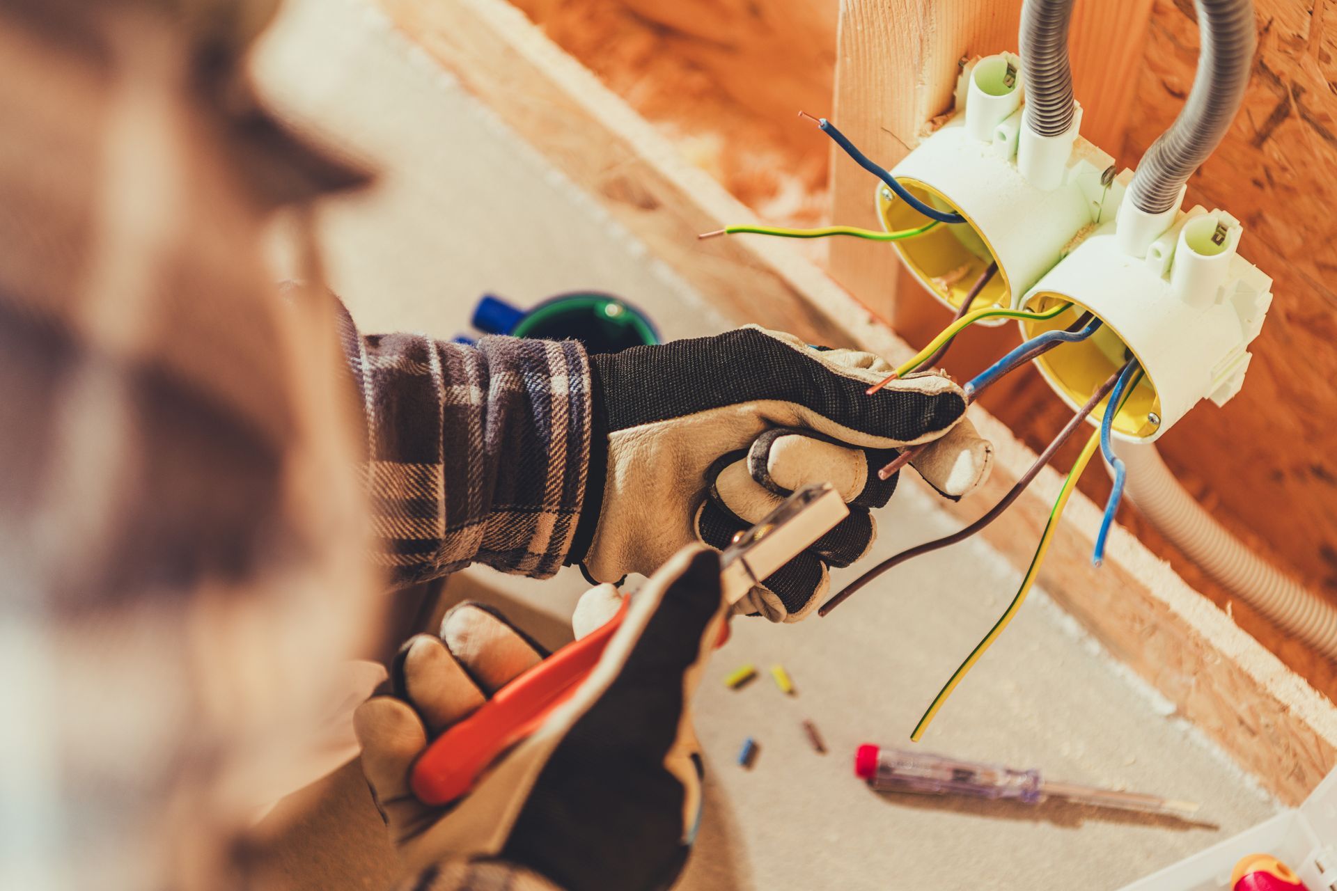 Electrician working on exposed wiring inside a wall box while using pliers and gloves.