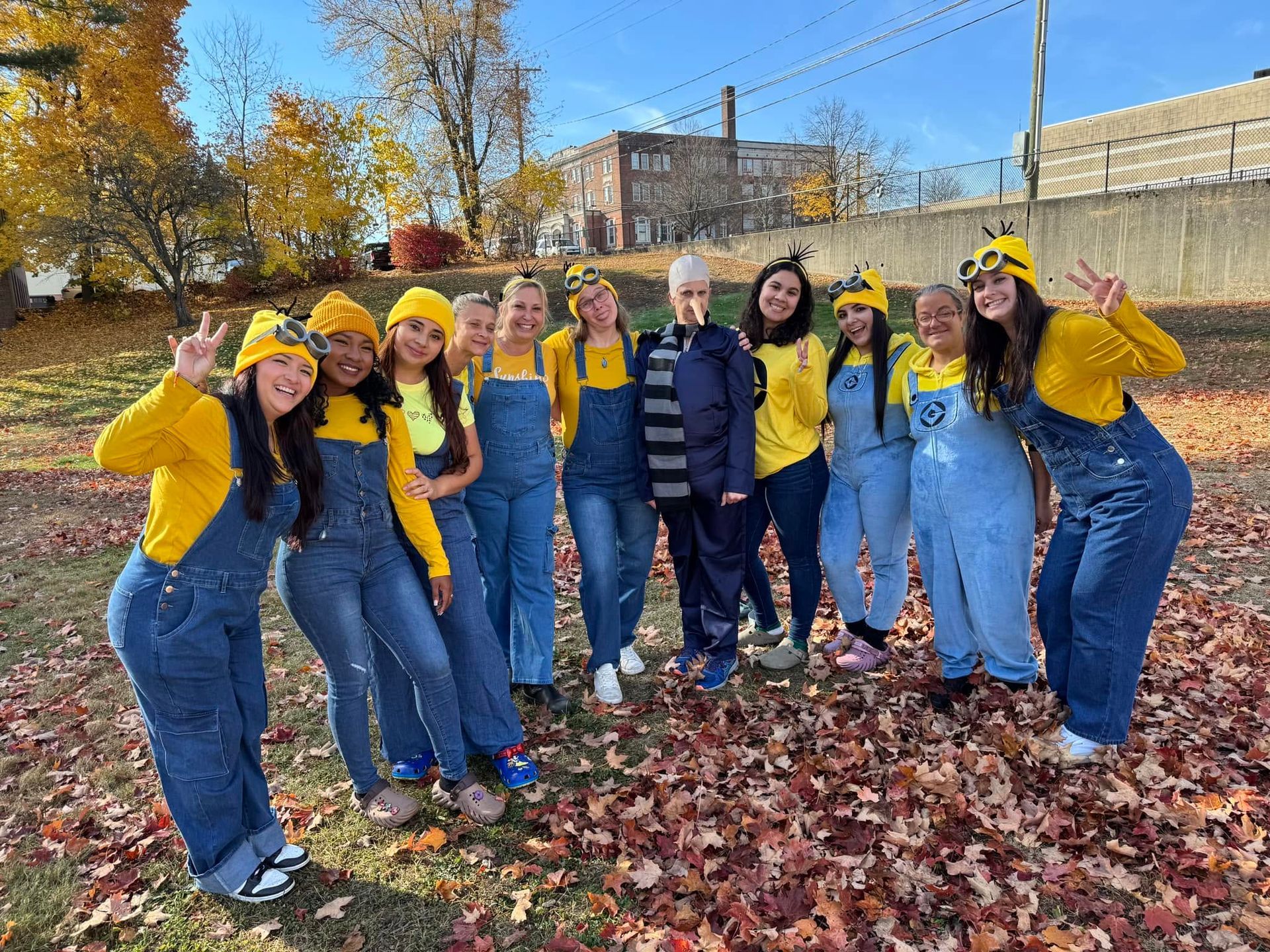 Group of people in yellow hats and blue outfits posing outdoors amid autumn leaves