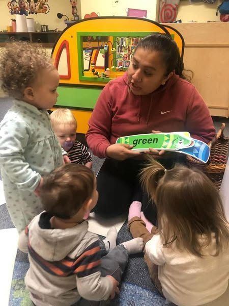 Teacher reading a green book to a small group of children in a classroom