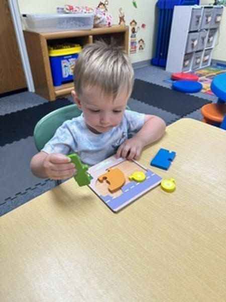 Child in a classroom table-top activity, placing a green puzzle piece on a colorful board.