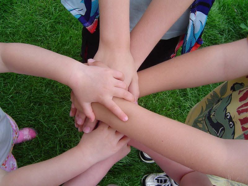 Children stacking hands together in a circle on grass outdoors