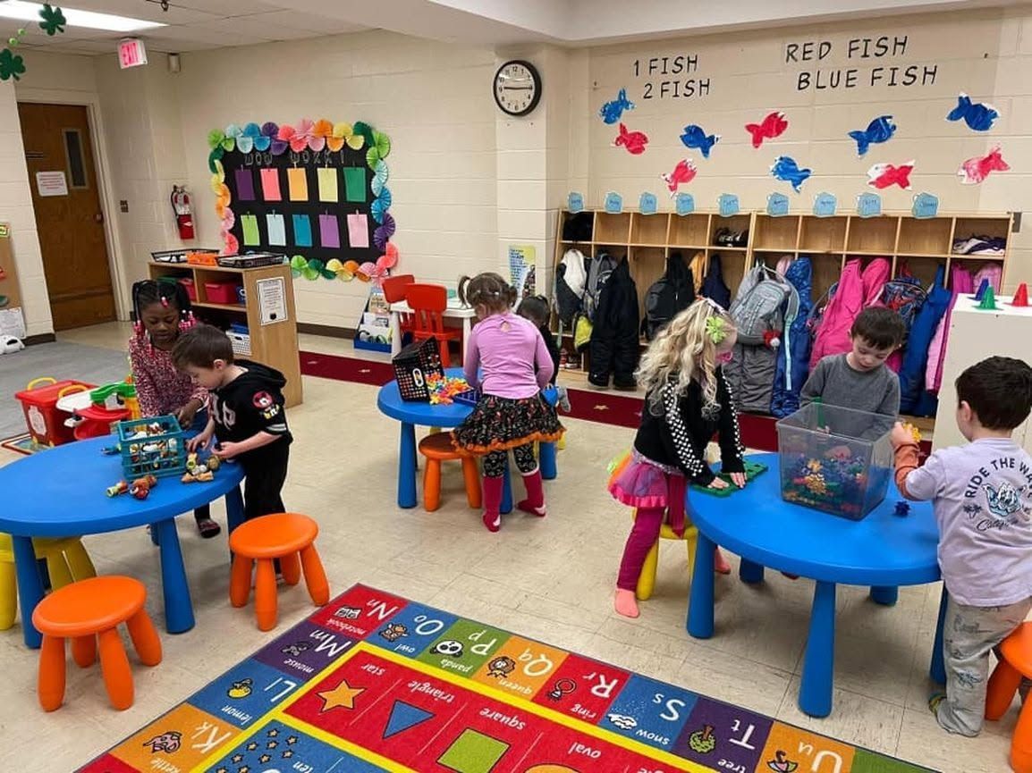 Children seated at colorful tables in a classroom, decorating crafts with supplies for a festive activity.